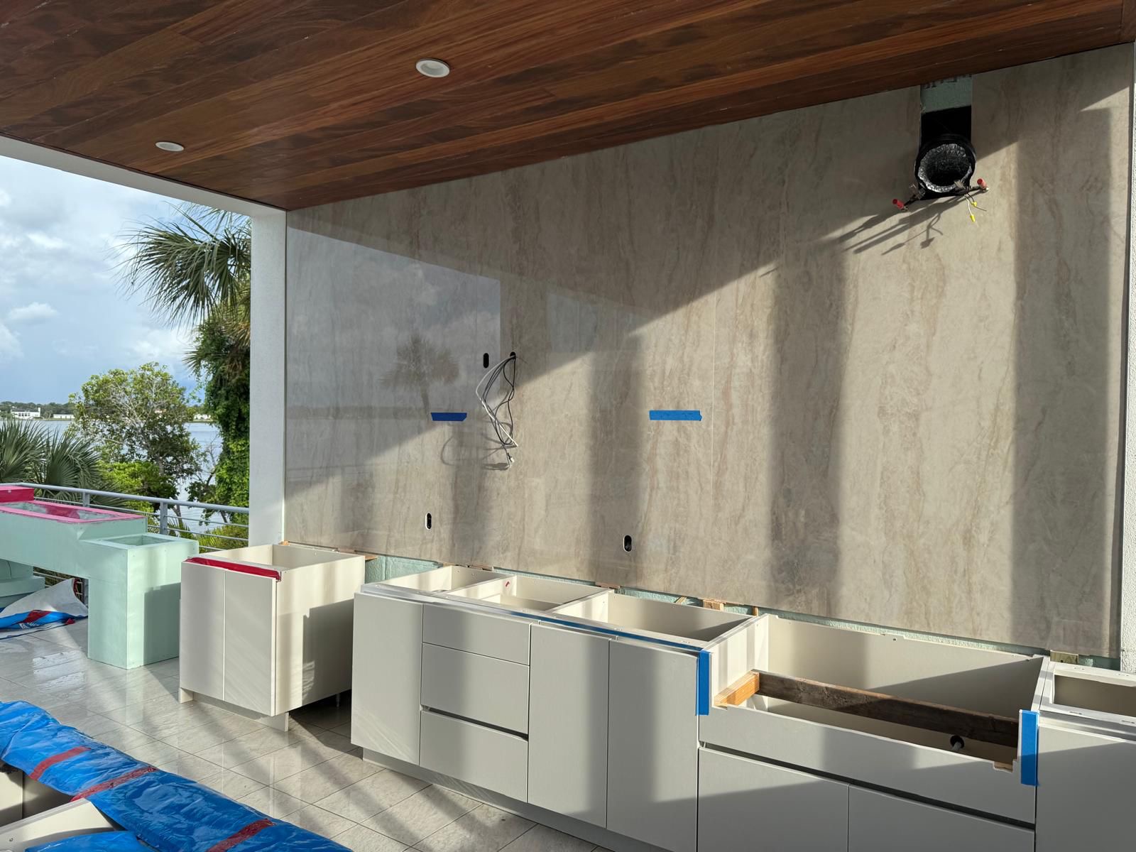 Outdoor kitchen cabinetry installation in progress beneath a wood ceiling with water views